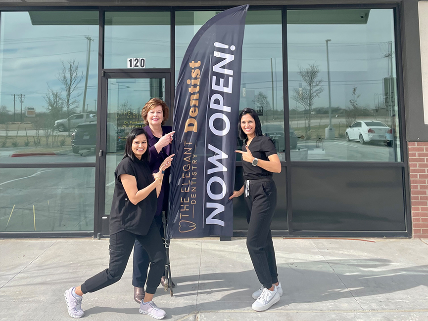 Three women outside pointing to advertisement sign