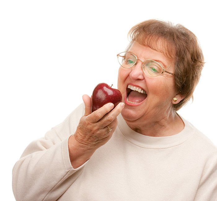 Older woman with dentures biting an apple