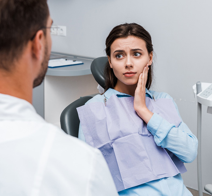 Concerned woman looking at emergency dentist while holding her cheek