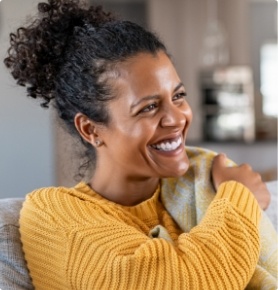 Smiling woman in yellow sweater sitting on couch