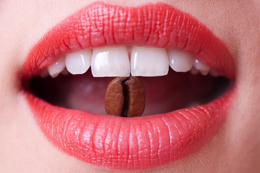 A woman’s teeth biting a coffee bean